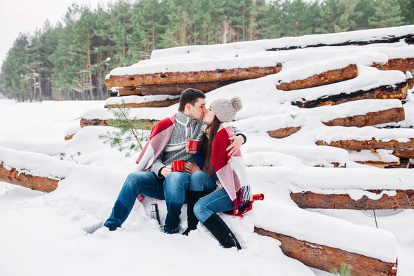 Casal sorridente envolto em um cobertor e beber chá ao ar livre na floresta de inverno — Fotografia de Stock