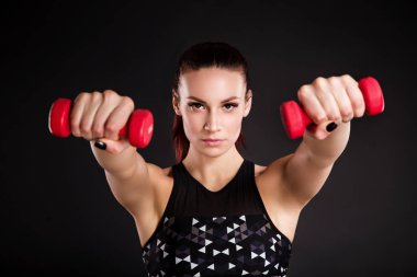 Güzel genç kadın dumbbells ile yapıyor. Fotoğraf siyah arka plan üzerine kusursuz bir beden ile atletik kadın. Güç ve motivasyon