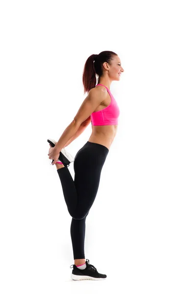 Unga fitness kvinna gör stretching hennes ben. Foto av muskulös kvinna i trendiga sportkläder på vit bakgrund. Styrka och motivation. — Stockfoto