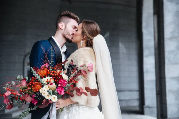 Knappe brunette bruidegom kussen van de mooie bruid in trouwjurk met boeket — Stockfoto