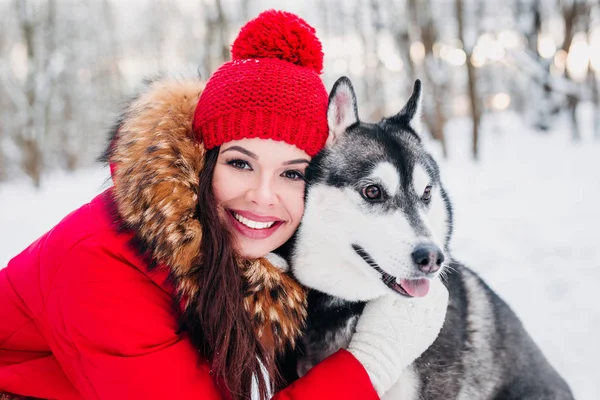 Mulher acaricia o cão Husky na floresta de inverno — Fotografia de Stock