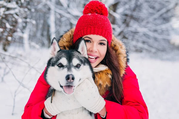 Mulher acaricia o cão Husky na floresta de inverno — Fotografia de Stock