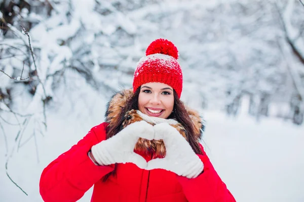 Mujer joven bastante romántica haciendo un gesto de corazón con los dedos delante de su pecho mostrando su amor en el fondo de invierno —  Fotos de Stock