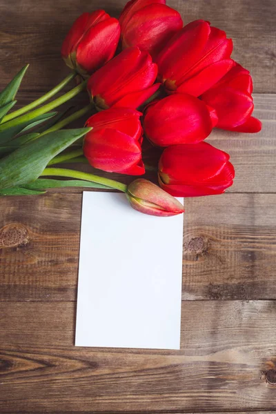 Flores da Primavera. Buquê de tulipas vermelhas com cartão para texto sobre fundo de madeira marrom. Conceito de Dia das Mães e Dia dos Namorados. Depósito plano — Fotografia de Stock