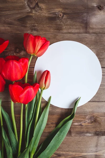 Flores da Primavera. Buquê de tulipas vermelhas com cartão para texto sobre fundo de madeira marrom. Conceito de Dia das Mães e Dia dos Namorados. Depósito plano — Fotografia de Stock