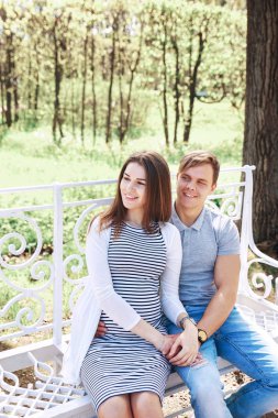 Gülümseyen hamile bir kadın oturmuş ve genç bir adam tarafından kucakladı