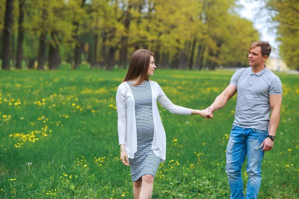 Mujer embarazada con marido caminando en el prado en el día de primavera — Foto de Stock