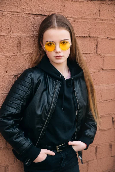 Jovem bela menina hipster elegante em óculos de sol e roupas casuais na parede marrom — Fotografia de Stock