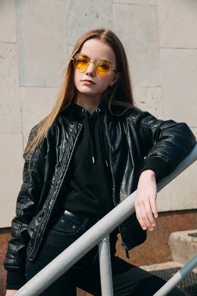 Fashion portrait pretty teenager girl in sunglasses and black rock style over city background