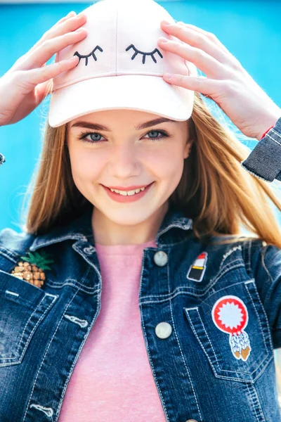 Ritratto primo piano bella adolescente sorridente in cappello e giacca di jeans sopra la parete blu — Foto Stock