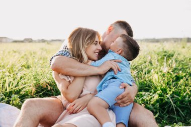 Mutlu aile yaz gününde birlikte zevk. Aile çim üzerinde oturan ve kucaklayan.