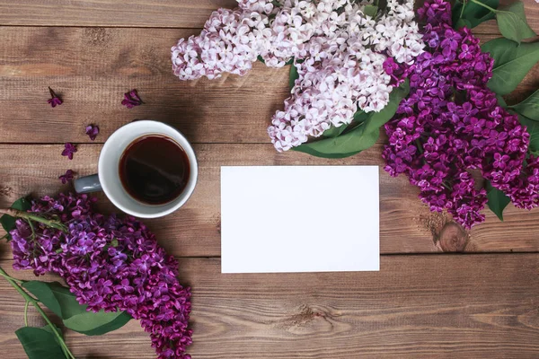 Ramo de flores lila sobre tablones de madera con tarjeta en blanco para texto y café. Vista superior — Foto de Stock