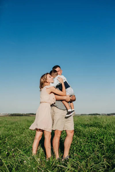 Familia feliz: padre joven, madre y su hijo pequeño caminando y abrazándose en el campo en el día de verano — Foto de Stock