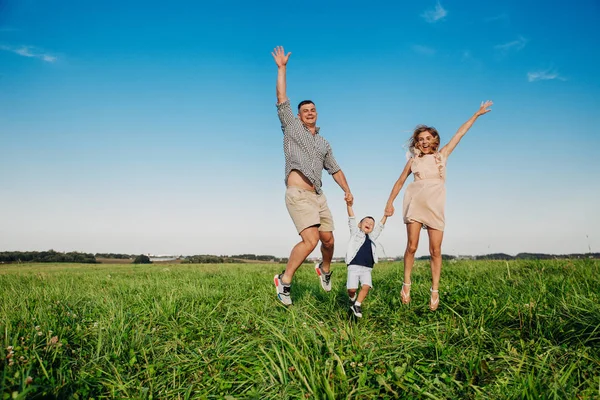 Lycklig familj hoppar tillsammans i fältet i solig dag — Stockfoto