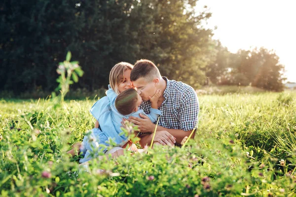 Familia feliz disfrutando juntos en el día de verano. Familia sentada y abrazándose en la hierba . — Foto de Stock