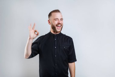 Close up portrait of cheerful handsome friendly man with modern hairstyle demonstrating ok symbol on gray background clipart