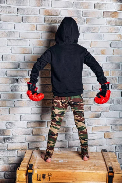 Little boy boxer with blonde hair dressing in black sweatshirt wearing boxing gloves posing in a studio.