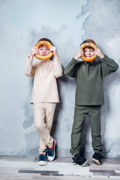 Little twin boys playing and dreaming of becoming a spaceman. Portrait of funny kids with bagels on gray wall