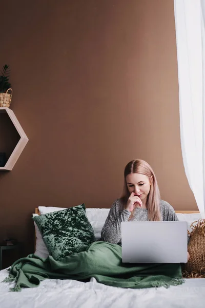 Mujer joven trabajando en la computadora en la cama. Relajarse en casa . — Foto de Stock