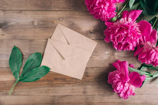 Ambachtelijke enveloppen en een boeket van Pioenen op een houten achtergrond — Stockfoto