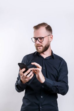 Gözlük Genç sakallı adam, modern akıllı telefon tutar, mesaj almak için mutlu, Casual siyah gömlek giymiş,