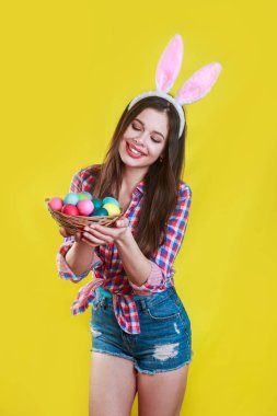 Sarı giyen tavşan kulakları yumurta ile sepet tutan genç neşeli kadın stüdyosu