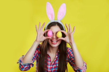 Tavşan kulağı takan ve gözlerinin önünde renkli bir Paskalya yumurtası tutan mutlu genç bir kadının stüdyo fotoğrafı.