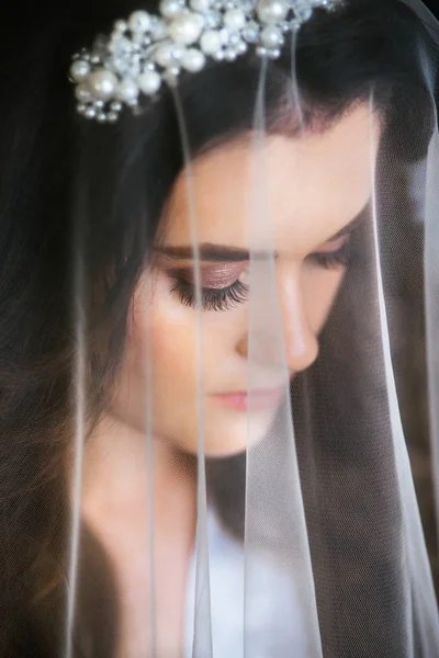 Hermosa novia joven con maquillaje de boda y peinado en el dormitorio. Hermoso retrato de novia con velo sobre su cara — Foto de Stock