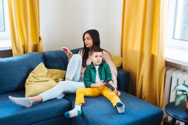 Anne, phona ve oğlunu TV izlerken kullanıyor. İnsanlar internet teknolojisi bağımlılığı kavramı