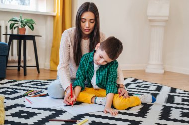 Güzel kadın ve onun sevimli küçük oğlu çiziyor ve yerde otururken gülümseyen