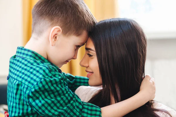 Beautiful mother and her cute little son looking at each other indoor — Stock Photo, Image