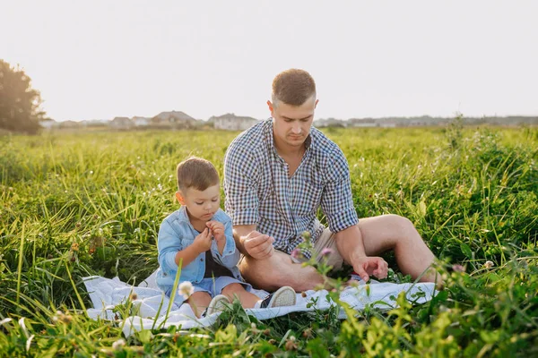 Smiling father and baby sitting on meadow in summer day — Stock Photo, Image