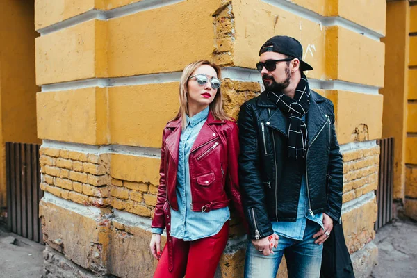 Sexy casal em jaqueta de couro e óculos de sol posando sobre a parede na cidade — Fotografia de Stock