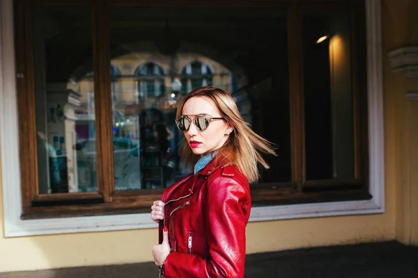 Retrato de moda de una joven bonita en chaqueta de cuero y gafas de sol posando en la ciudad — Foto de Stock