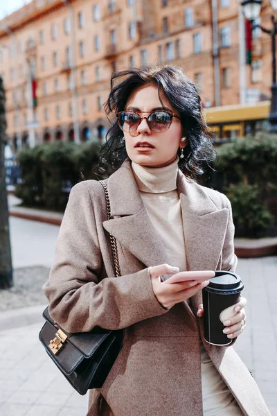 Модная деловая женщина пьет кофе и пишет смс на улице — стоковое фото