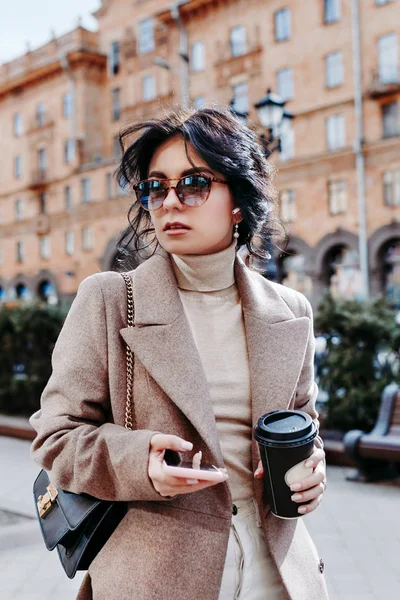 Fashionable businesswoman drinking coffee and texting outdoors in city street — Stock Photo, Image