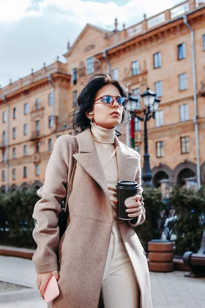 Красивая молодая женщина на городской улице с мобильным телефоном и кофе — стоковое фото