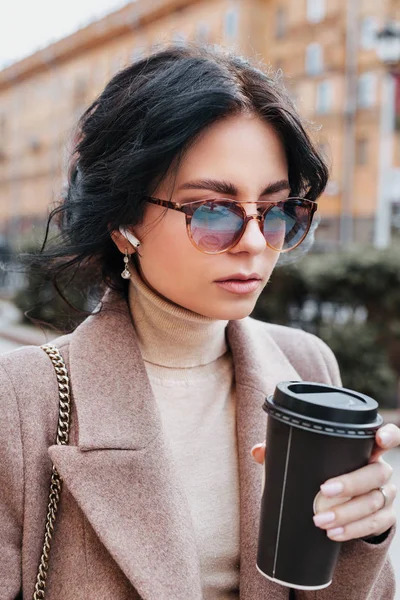 Beautiful young woman drinking coffee while walking along the street. Coffee on the go