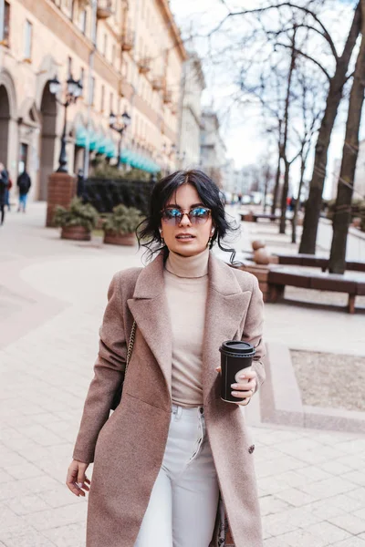 Женщина держит бумажную чашку кофе и наслаждается прогулкой по городу — стоковое фото