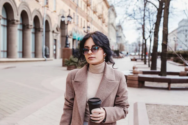 Elinde kağıt kahve fincanı tutan ve şehirde yürüyüşün tadını çıkaran güzel bir kadın. — Stok fotoğraf