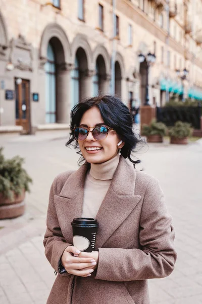 Lifestyle fashion portrait of young stylish woman walking on the street and drinking coffee — Stock Photo, Image