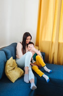 Güzel genç anne ve küçük oğlu bir akıllı telefon kullanarak ve evde kanepede otururken gülümseyerek