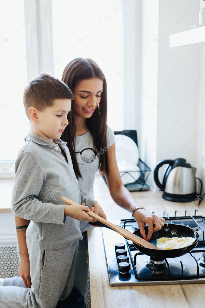 Beautiful young mother with her little son is cooking in the kitchen at home