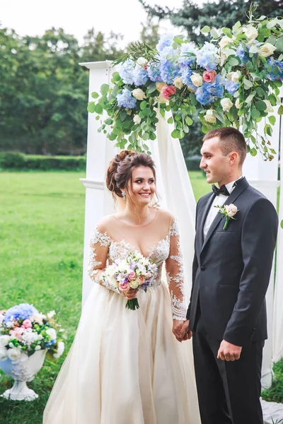 Casal de casamento bonito perto do arco de casamento ao ar livre . — Fotografia de Stock