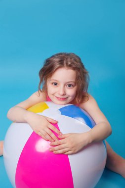 Mavi arka plan üzerinde büyük şişme topu ile küçük gülümseyen kız