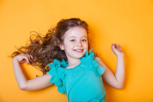 Linda niña de 7 años en blusa azul acostada sobre fondo naranja — Foto de Stock