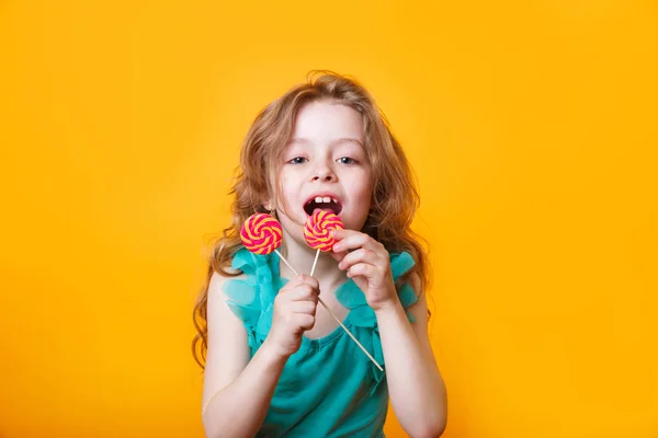Funny child with candy lollipop, happy little girl eating big sugar lollipop on yellow bright background, — Stock Photo, Image