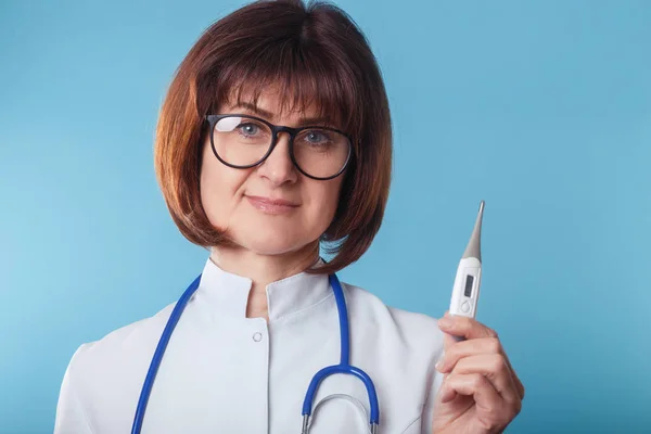 Lekarz kobieta pokazując termometr na niebieskim tle — Zdjęcie stockowe