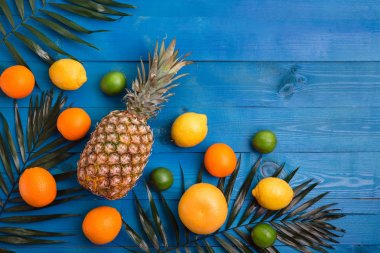 Ananas, portakal, limon, greyfurt, limon ve palmiye yaprakları mavi ahşap arka plan üzerinde