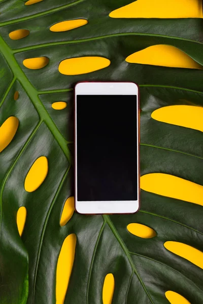 Teléfono inteligente sobre un fondo amarillo de hojas de palma  . — Foto de Stock